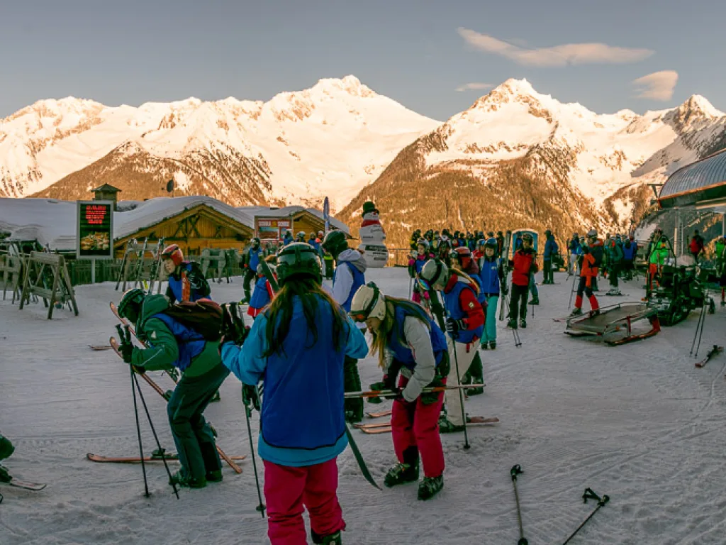 Skifahrende an der Talstation im Abendlicht.